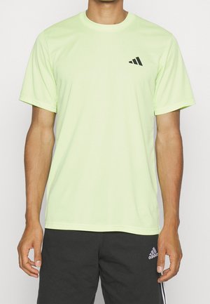 Mann trägt hellgelbes Adidas T-Shirt und schwarze Adidas Shorts mit sichtbaren Logos auf beiden Kleidungsstücken.