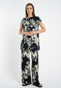 Czarny strój w kwiatowy wzór, składający się z tuniki z krótkim rękawem oraz spodni o szerokich nogawkach, wykonany z gładkiego, lekkiego materiału. Całość dopełniają płaskie sandały.