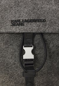 Juodas ir pilkas kuprinė su tekstūriniu paviršiumi, kurioje yra "KARL LAGERFELD JEANS" logotipas ir sidabrinė sagtis viršuje.