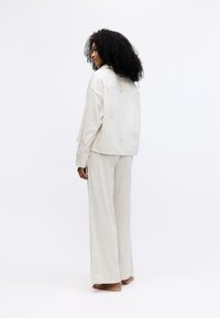 Lichtbeige, textuurde twee-delig outfit bestaat uit een oversized blouse met een verlaagde schouder en wijde broekspijpen. Minimalistisch ontwerp, zonder zichtbare sluitingen.
