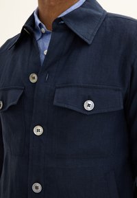 Navy blue button-up jacket made of textured fabric, featuring a pointed collar, two chest pockets, and silver-tone buttons.
