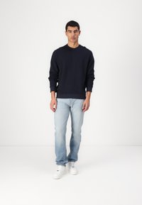 Sudadera azul marino con cuello redondo, combinada con jeans celestes. Modelo lleva zapatillas blancas. Diseño simple y casual.
