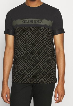 Black T-shirt featuring a patterned lower half, solid black upper with olive green panel and "GLORIOUS" text in bold, textured fabric accents.