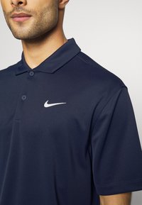 Nike Polohemd in Marineblau, aus einem glatten Stoff gefertigt. Verfügt über einen umschlagbaren Kragen, eine zwei-Knopf-Leiste und ein weißes Logo auf der Brust.