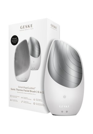 Geske 6-i-1 hvid sonisk termisk ansigtsbørste med tekstureret silikoneoverflade og varmeplade, vist ved siden af sin produktæske.