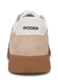 Ljusbeige mockasneaker med vita meshinslag, brun "WODEN"-logga och en brun gummisula. Texturerad yta på ovandelen.