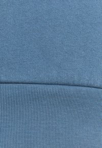 Gros plan d’un tissu tricoté bleu plié montrant un fin côtes verticales et une texture tricotée lisse avec une ligne de couture horizontale.