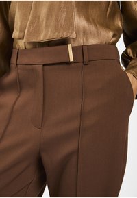 Bruine op maat gemaakte broek met een gladde textuur, voorzien van een stijlvolle tailleband en een accenten in gouden tint. De stof heeft een subtiele glans.