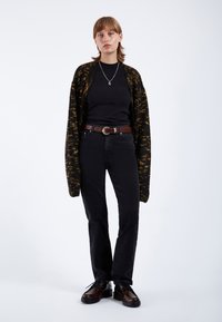 Jeans neri, t-shirt nera e un cardigan a righe nere e gialle. Una cintura marrone e scarpe scure con tacco basso completano l'outfit.