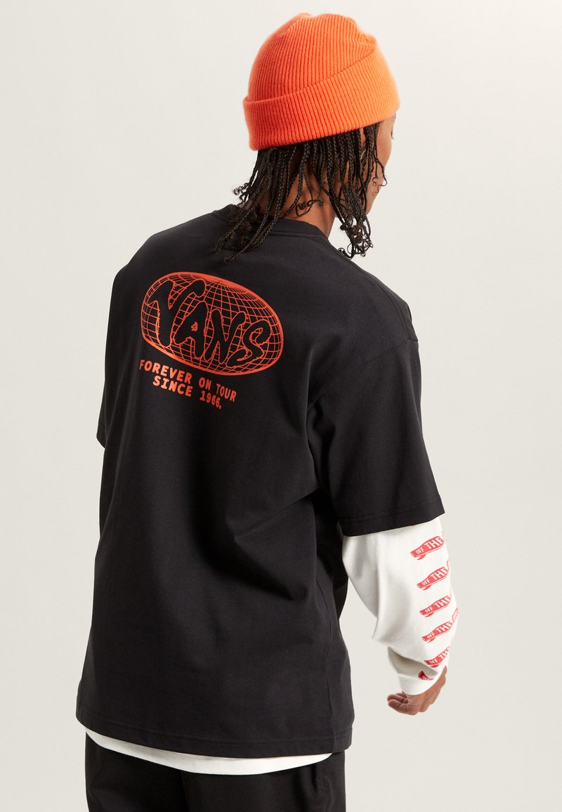 Svart bomullströja med röd grafisk design på ryggen som säger "Vans" och "Forever on Tour." Lager med en vit långärmad skjorta under.