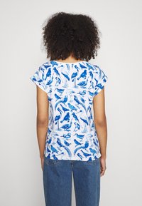 Cotton t-shirt featuring a blue bird pattern on a white background, with short sleeves and a relaxed fit. Rear view shows design detail.