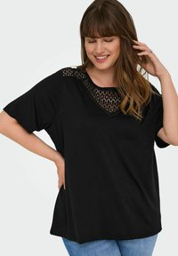 Svart kortärmad topp med en spetspanel vid halslinningen, med avslappnad passform och mjukt tyg. I kombination med ljusblå denim.