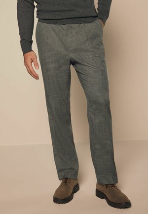 Grau karierte Hose mit lässiger Passform, ausgestattet mit einem strukturierten Stoff und einem subtilen Muster. Kombiniert mit braunen Schuhen für einen stimmigen Look.