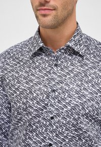 Uomo che indossa una camicia a maniche lunghe bianca e nera con un motivo di varie illustrazioni di auto nere.