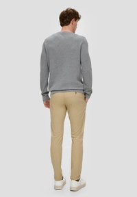 Pull en tricot gris à manches longues, col rond ; associé à un pantalon chino beige et des baskets blanches. Vue arrière de la tenue.