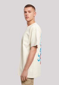 Korte mouwen, crèmekleurig katoenen t-shirt met een kleurrijk graphic ontwerp op de achterkant, met blauwe en rode accenten.