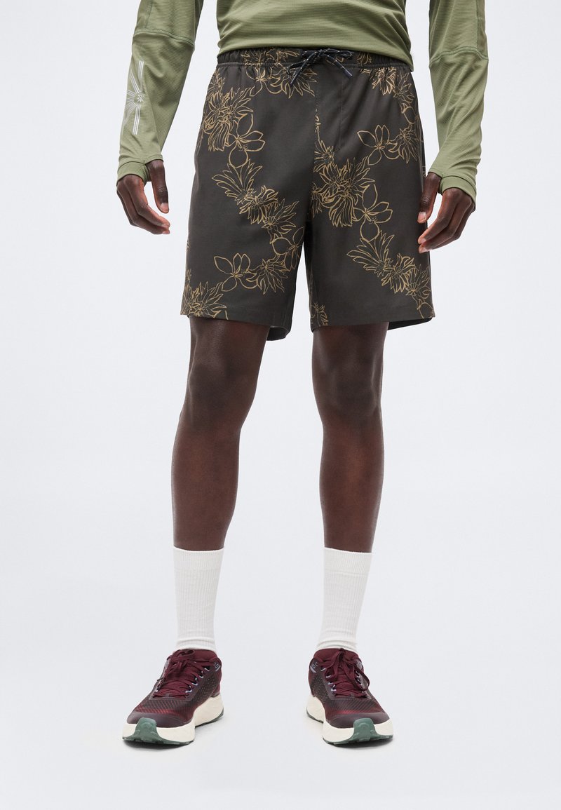 Ανδρικά πόδια με μαύρα σορτς με λουλουδένιο σχέδιο, λευκές κάλτσες, μπορντό αθλητικά παπούτσια και ελιάς πράσινο μακρυμάνικο πουκάμισο.