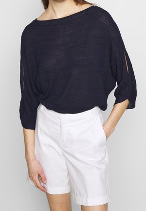 Marineblauwe, lose knit-top met een brede halslijn en 3/4 mouwen. Gecombineerd met witte shorts. Gestructureerde, lichte stof.