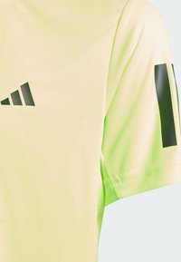 T-shirt de sport à manches courtes en jaune fluo et vert clair. Présente un logo noir et des accents noirs contrastants sur les épaules. Texture lisse.