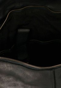 Interno di una borsa a tracolla nera in pelle, con chiusura a zip, texture liscia e un piccolo manico in pelle. L'imbottitura appare scura e priva di decorazioni.