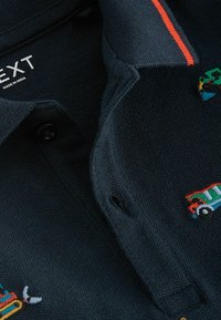 Marinblå piké skjorta med texturerat tyg, pryd med färgglada broderade mönster, en röd accent på kragen och knappknäppning.