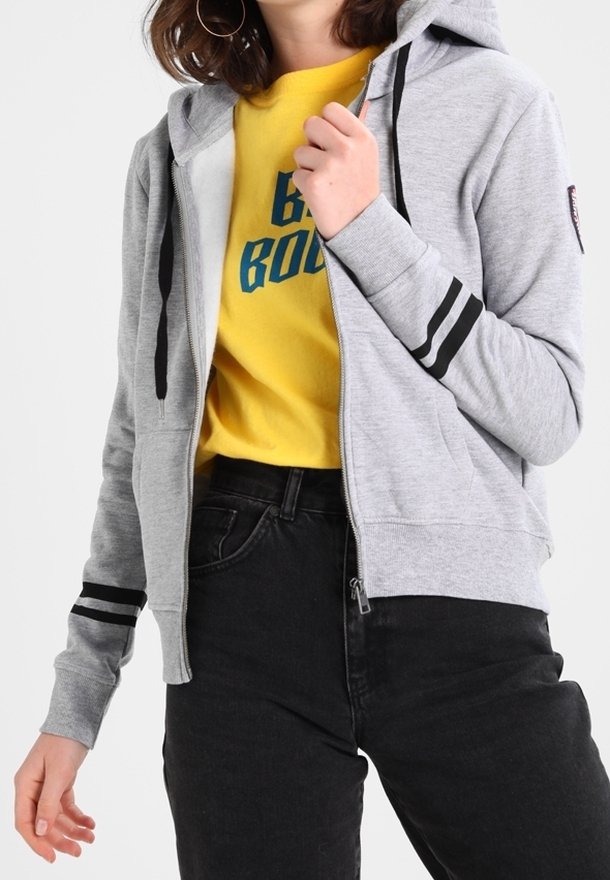 Grauer Baumwoll-Hoodie mit Reißverschluss und schwarzen Streifen an den Ärmeln, kombiniert mit einem gelben T-Shirt mit Grafik und schwarzer Jeans. Verfügt über eine Kapuze mit Kordelzug.