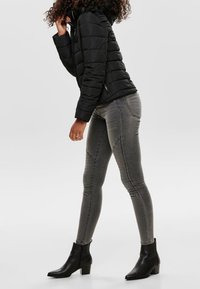 Svart puffjacka med horisontella sömmar, grå skinny jeans med ribbade detaljer och svarta ankelstövlar med låg blockklack.