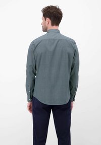 Herenoverhemd van donkergroene stof met een klein geometrisch patroon, voorzien van een puntkraag, knoopmanchetten en een gebogen zoom.