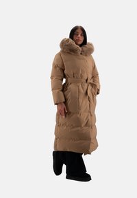 Lang, beige puffermantel med en faux fur krave, bælte i taljen og sidelommer. Har en quiltet struktur og en løs pasform.