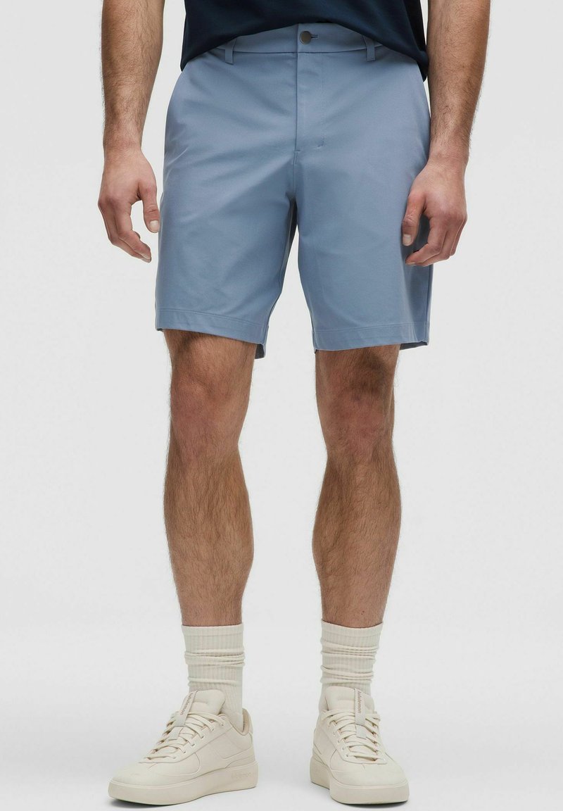 Heledad sinine lühike püksid siledast materjalist, millel on lame esipind, küljetaskud ja nupuga sulgus. Kombineeritud valgete tossude ja sokkidega.