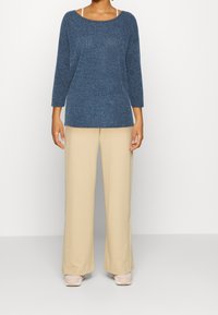 Top blu textured a maniche lunghe con scollatura ampia, abbinato a pantaloni beige a gamba larga. Entrambi i capi presentano una vestibilità comoda.