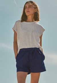 Camisa de rayas de manga corta con puños enrollados, combinada con pantalones cortos azul marino que tienen una cinturilla elástica y cordón. Un atuendo casual de verano.