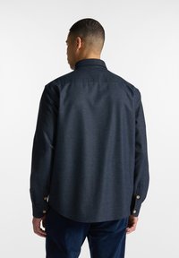 Navyblauwe overhemdd met een gestructureerde afwerking, lange mouwen en een ronde zoom. Heeft knopenmanchetten en een standaard kraag.