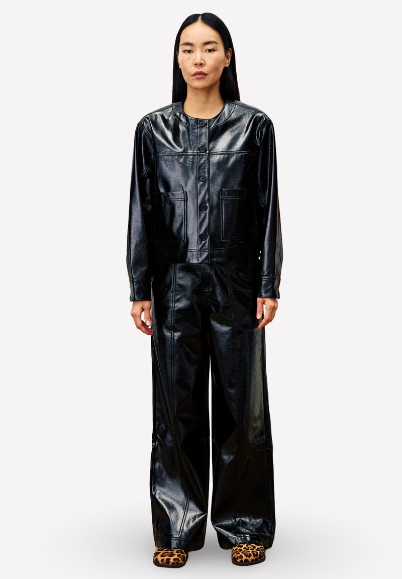 Veste en simili cuir noir avec col de chemise, fermeture à boutons et poches avant, associée à un pantalon large assorti. Chaussures à imprimé léopard.