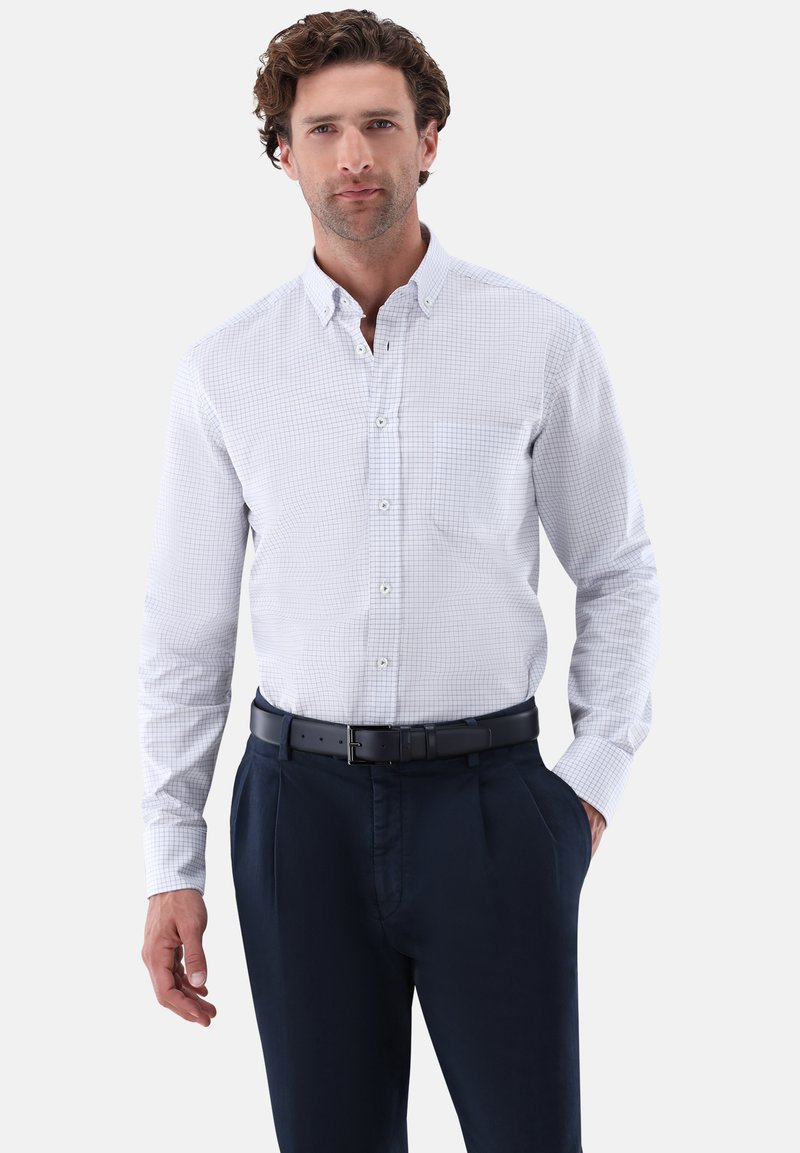 Long-sleeve button-up shirt in white with a blue check pattern, featuring a pocket and a collar. Worn with navy trousers and a black belt.