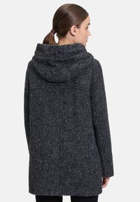 Czarnoszary płaszcz z fakturowanej wełny z kapturem, o luźnym kroju i średniej długości, z widocznymi detalami szwów na plecach.