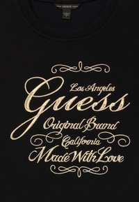 Juodas džemperis su auksiniu siuvinėjimu, kuriame užrašyta "Guess", "Los Andželas", "Originali Prekė", "Kalifornija" ir "Pagaminta su meile".
