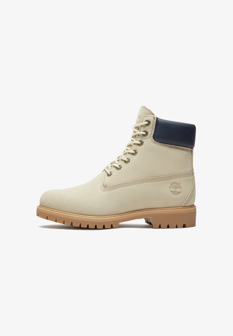 Beiger Schnürstiefel mit gepolstertem schwarzem Kragen, robuster hellbrauner Sohle und geprägt gestaltetem Baum-Logo an der Außenseite.