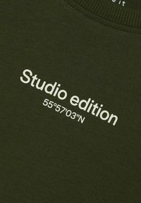 Oliven grønn hettegenser med hvit tekst som leser "Studio edition 55°57'03''N" på forsiden. Glatt tekstur med ribbet halsåpning.