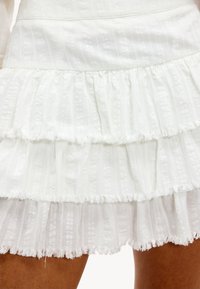 Witte tiered rok gemaakt van textuurstof met franjes aan de randen, met subtiele verticale strepen en een gerimpelde zoom.
