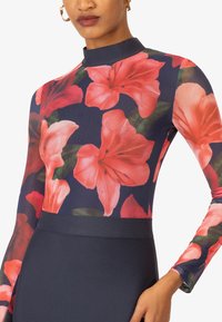 Abito a maniche lunghe con un motivo floreale con fiori rosa e rossi su uno sfondo blu navy. Tessuto texturizzato con corpino aderente e colletto alto.