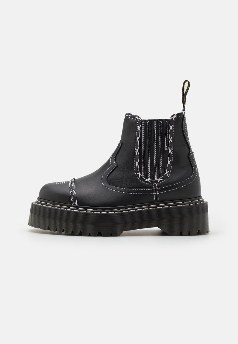Bottine noire en cuir avec semelle épaisse, coutures contrastantes blanches, panneau latéral élastique et languette à l'arrière.