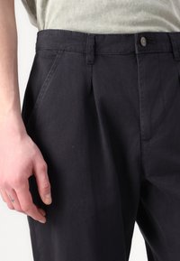 Marinblå byxor med veck, tillverkade av bomullsmaterial med blandning. Har en knäppning med knapp och sidofickor. Texturerad tyg med en slät finish.