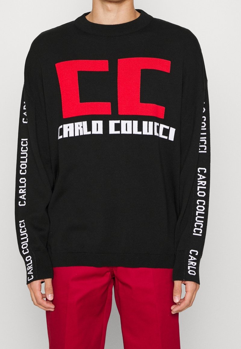Czarny sweter z dużym czerwonym logo "CC" i napisem "CARLO COLUCCI" w białym kolorze na rękawach. Rybaczka dekolt i mankiety. Gładka faktura.