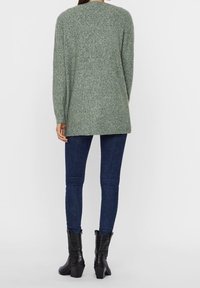 Green knit sweater with long sleeves, rounded neckline, and a relaxed fit, paired with dark blue skinny jeans and black heeled boots.