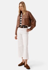 Brązowa skórzana kurtka o kroju cropped z dwoma przednimi kieszeniami, zestawiona z pasiastą koszulą, białymi spodniami typu wide-leg i brązowymi zamszowymi loafersami.