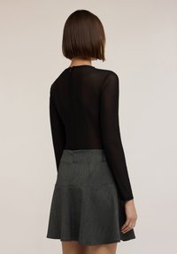 Schwarzer Langarm-Body mit transparenter Textur, kombiniert mit einem grauen, ausgestellt geschnittenen Rock mit dezentem Muster und rückseitigem Reißverschluss.