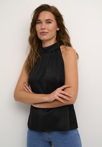 Black sleeveless top with a high neck, featuring a textured fabric and relaxed fit. Paired with blue denim jeans.