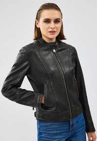 Giacca di pelle nera con collo alla coreana, chiusura con zip e tasche laterali con zip, dotata di una finitura leggermente testurizzata e un design aderente.