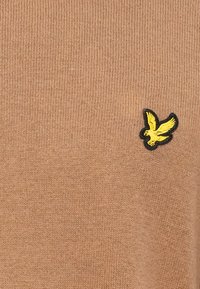 Beige kötött pulóver, amelynek bal oldalán egy apró fekete és sárga hímzett madárlogó található. Puha tapintású, bordázott dizájnnal.